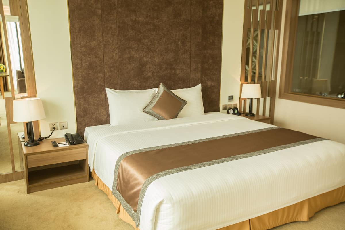 A hotel room with a large bed, a wooden headboard, bedside lamps, a nightstand with a phone, and a mirror.