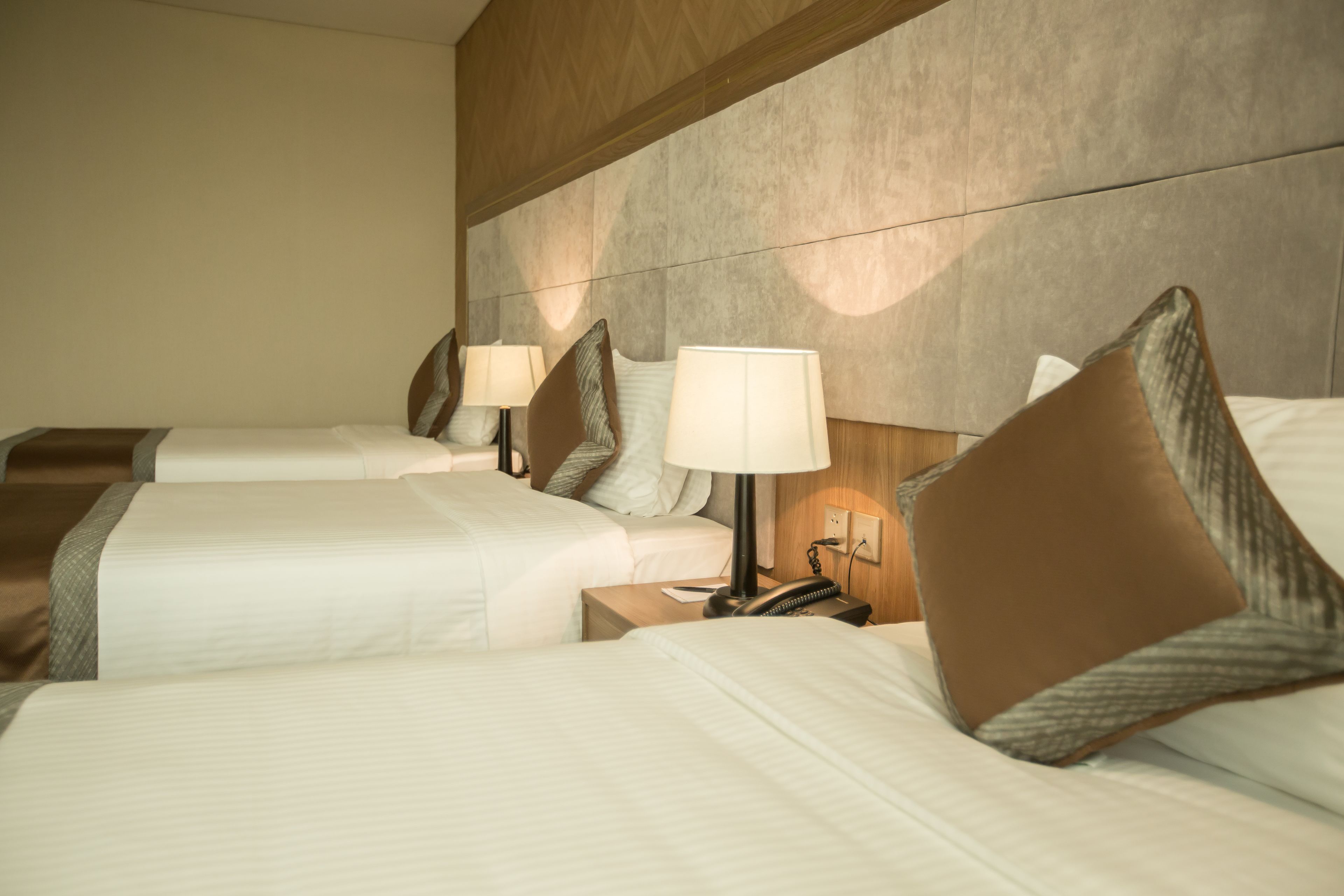 A hotel room with three beds, each with a pillow and a bedside lamp.
