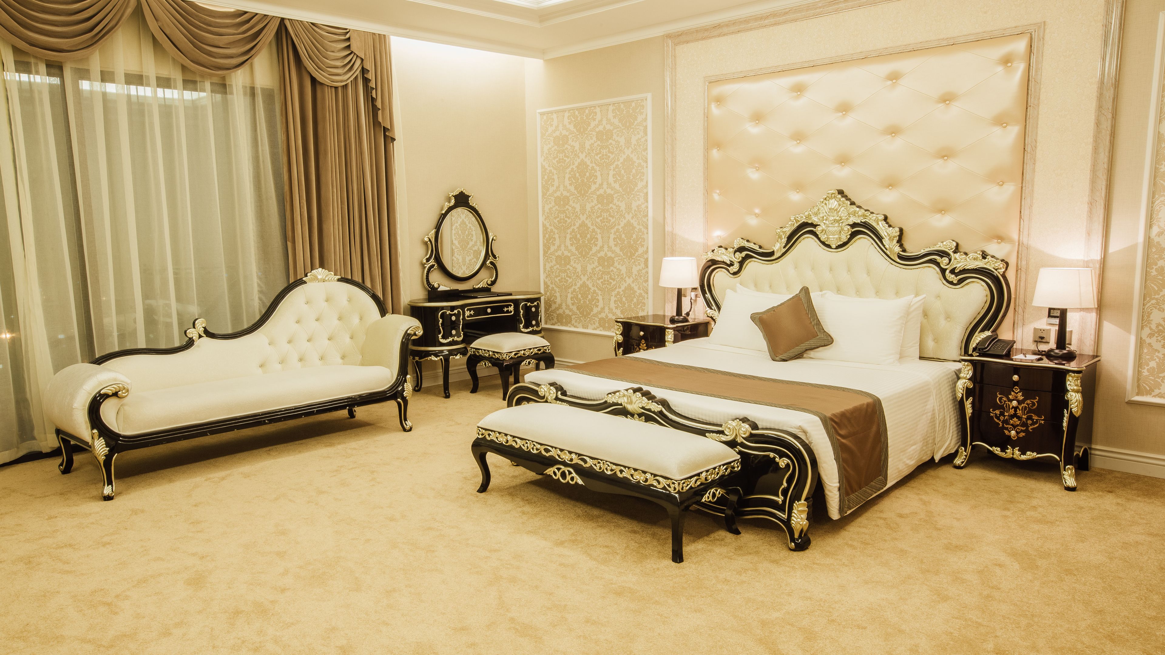 Un dormitorio lujoso con una cama grande, un chaise lounge y una mesita de noche con lámpara.