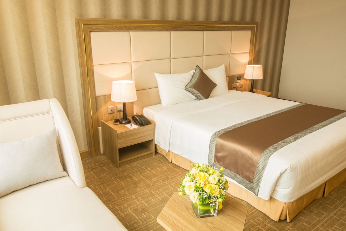 A hotel room with a large bed, two bedside tables, a nightstand, a chair, and a vase of flowers.