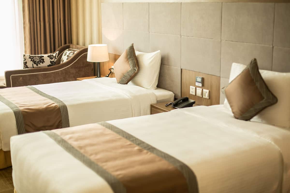 A hotel room with two beds, a sofa, a lamp, a phone, and a wall-mounted thermostat.
