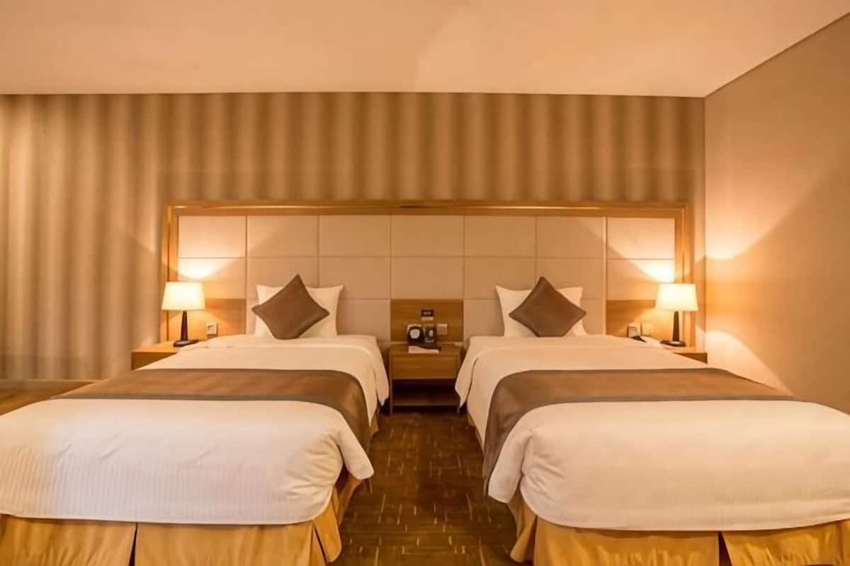 A hotel room with two beds, a headboard, bedside tables, lamps, and a radio.