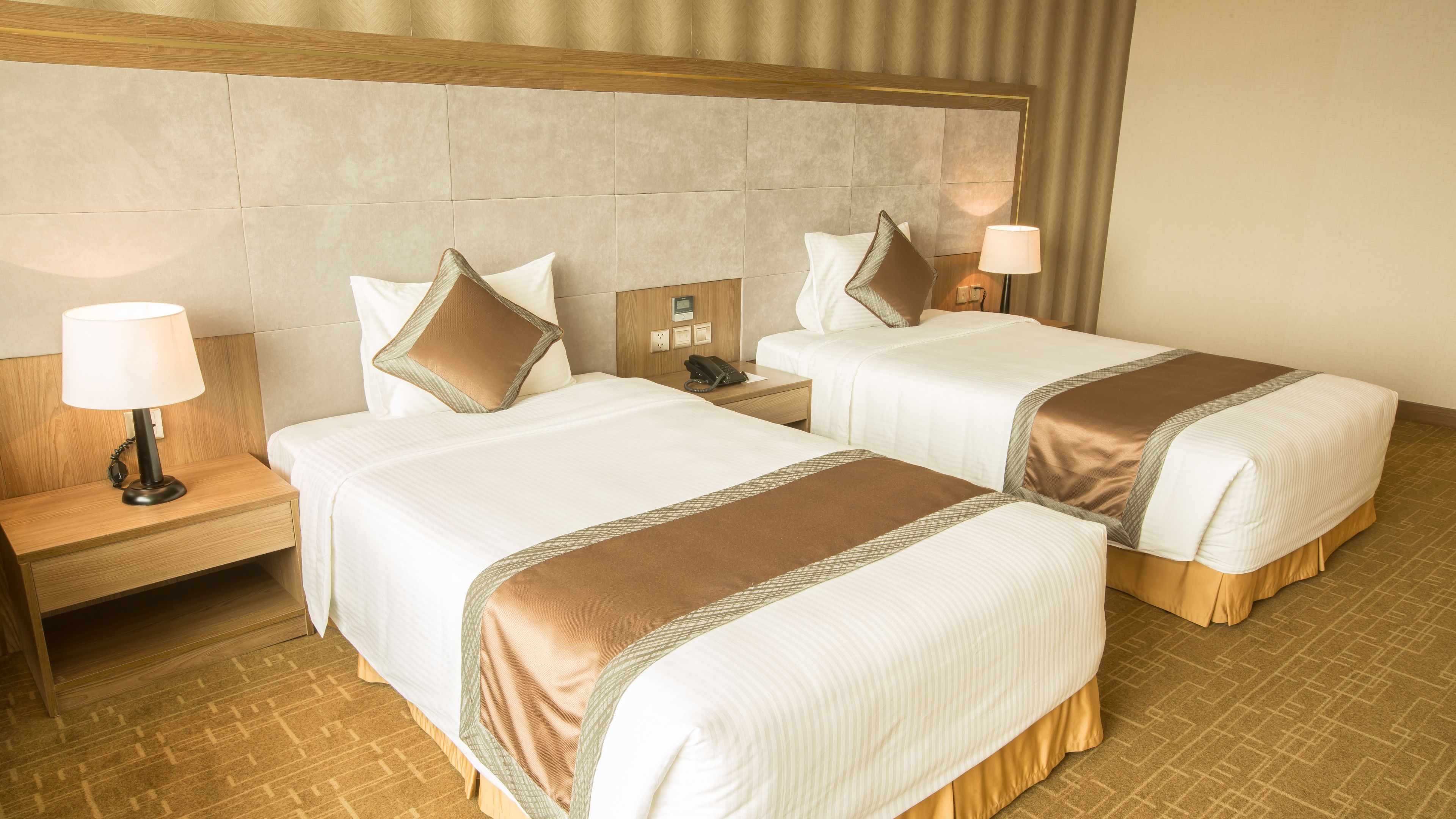 A hotel room with two beds, a wooden headboard, bedside lamps, and a patterned carpet.