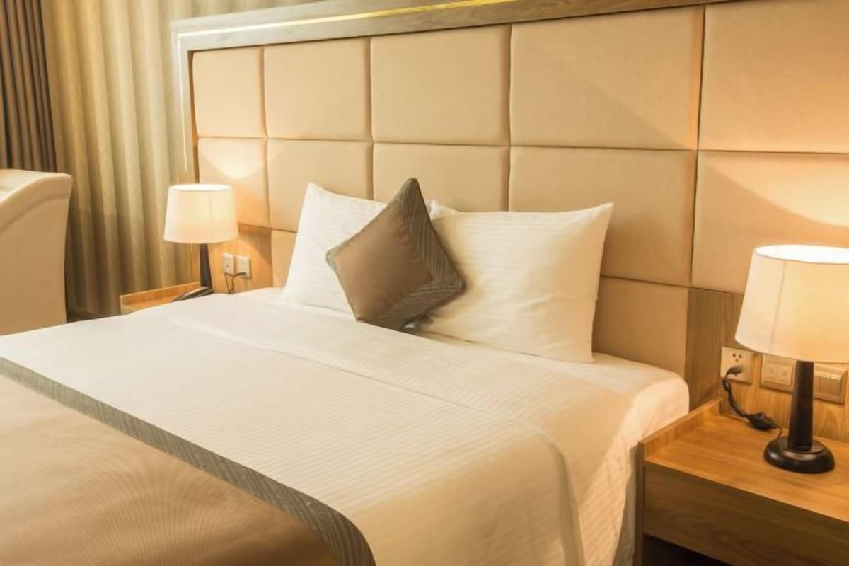 A hotel room with a large bed, a headboard, two bedside tables with lamps, and a curtain.