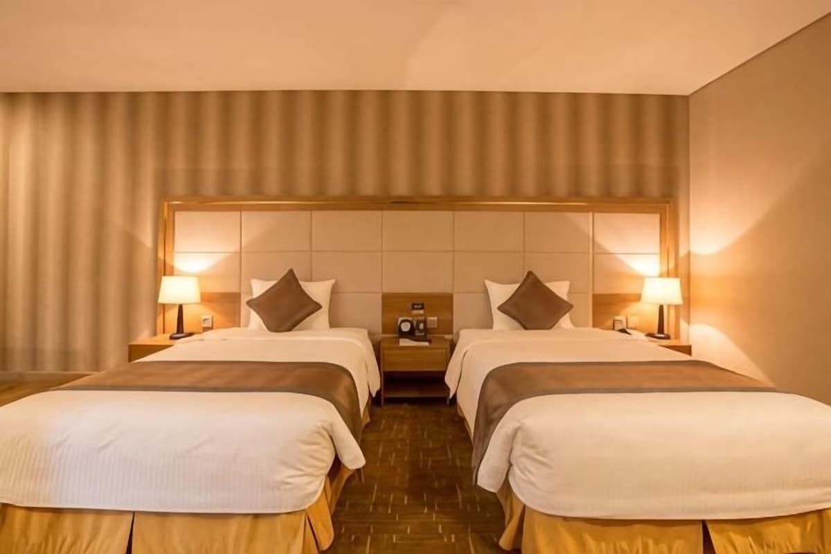 A hotel room with two beds, a headboard, bedside tables, lamps, and a radio.