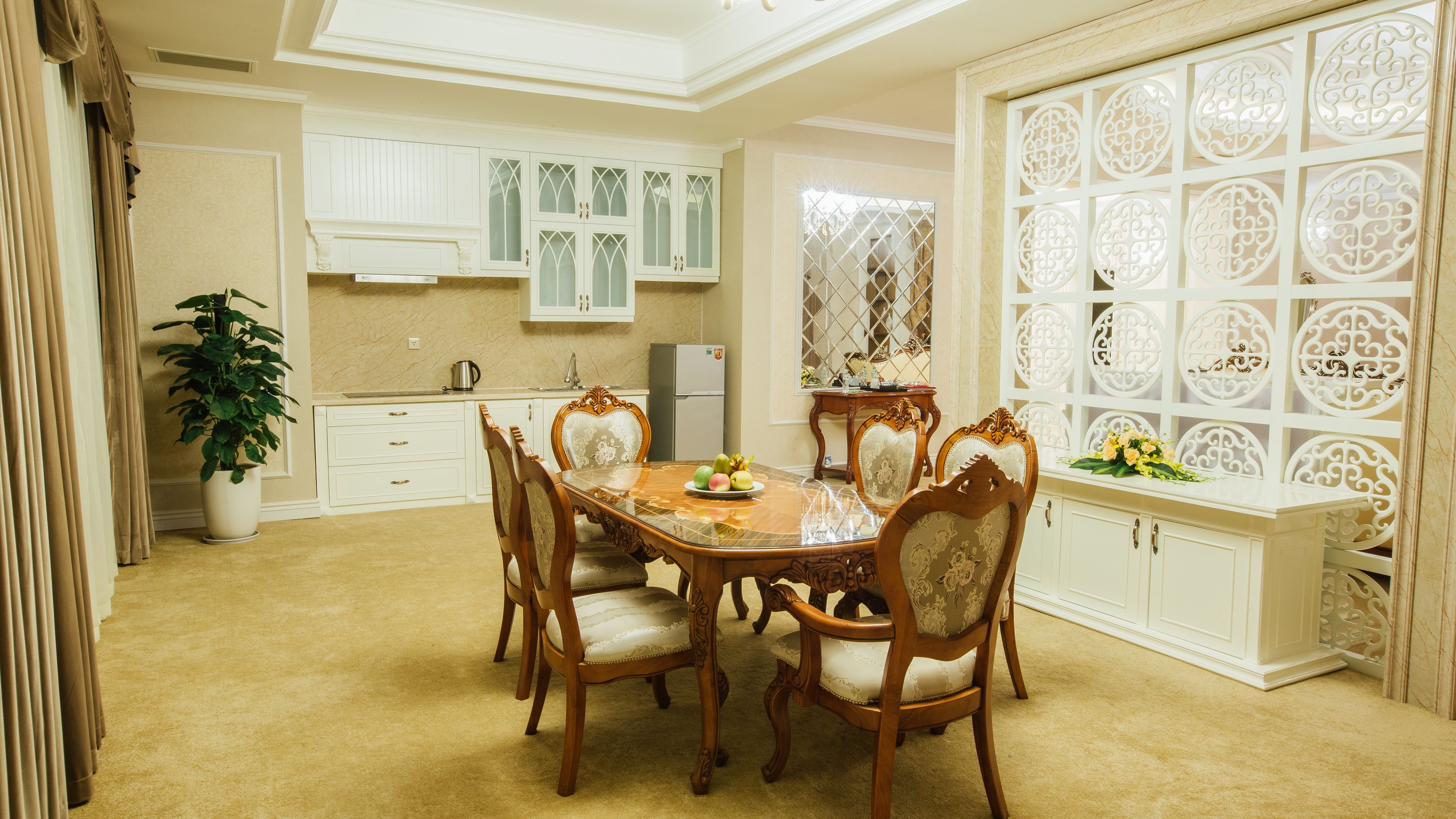 A dining area with a wooden table and chairs, a potted plant, and a decorative window with intricate patterns.