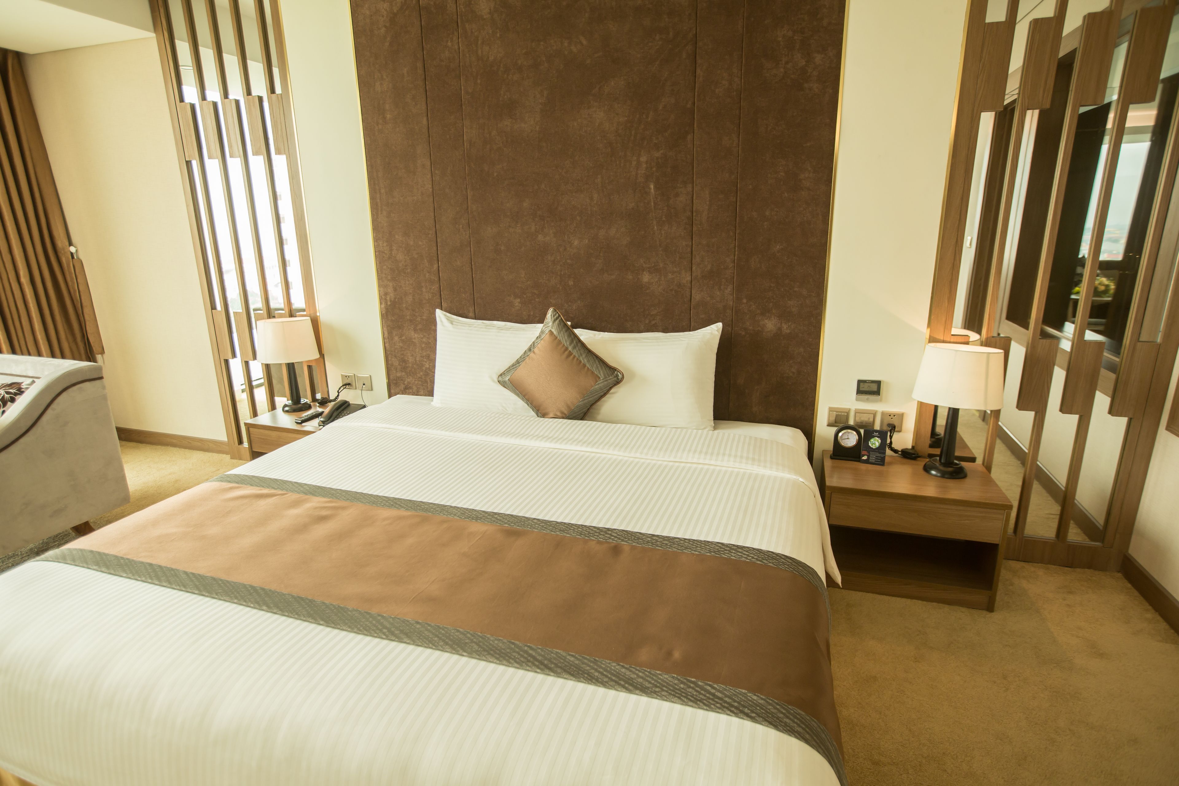 A hotel room with a large bed, a nightstand, a lamp, and a mirror.