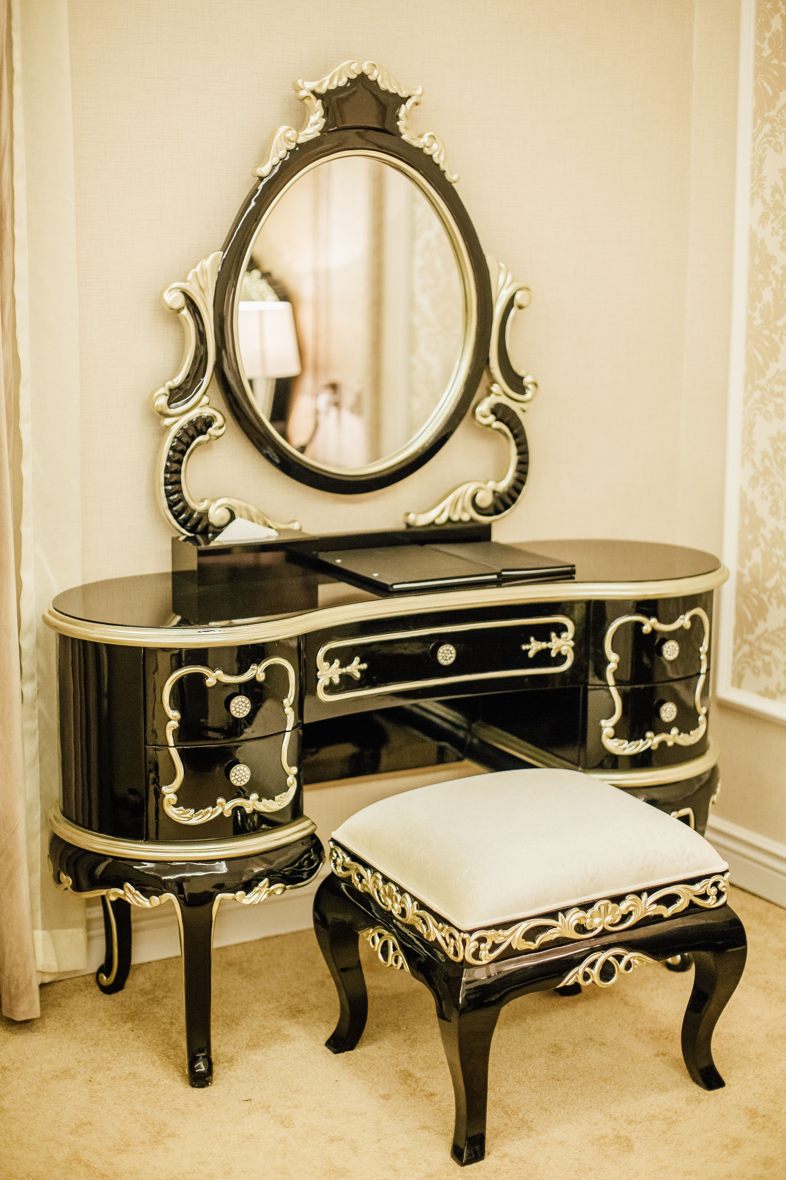 A black vanity with a mirror, a drawer, and a cushioned stool.