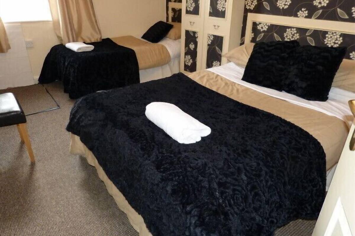 Habitación de hotel con dos camas, cada una con cubrecama negro y toalla blanca. La habitación tiene papel tapiz floral y cabecera de madera.