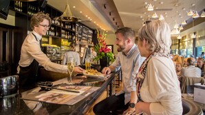 A bar area with a bartender serving drinks to customers seated at a table. - The Warwick Southport (Southport)