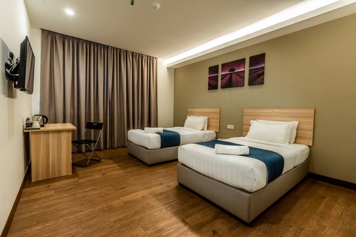 A hotel room with two beds, a desk, a chair, and a TV.