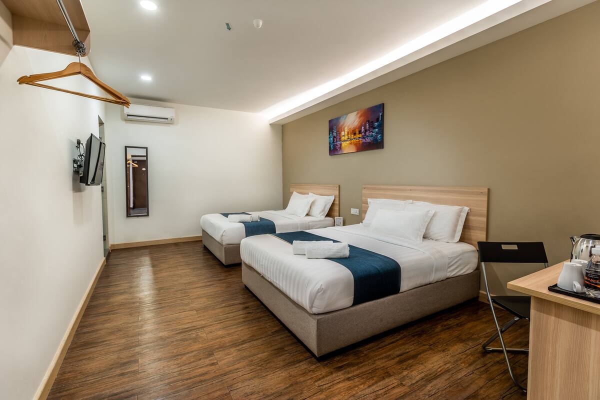 A hotel room with two beds, a desk with a coffee maker, and a painting on the wall.