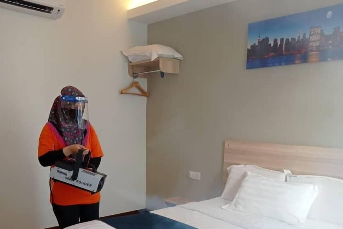 A hotel room with a bed, a white pillow, a blue blanket, a painting of a cityscape, and a person holding a luggage trolley.