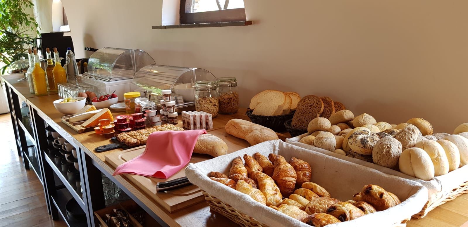 A breakfast buffet with various breads, pastries, and condiments.