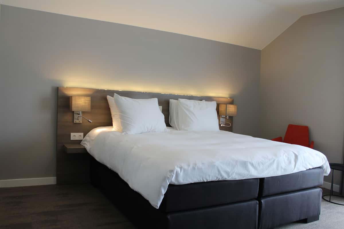 A modern hotel room with a large bed, two bedside lamps, and a red chair.