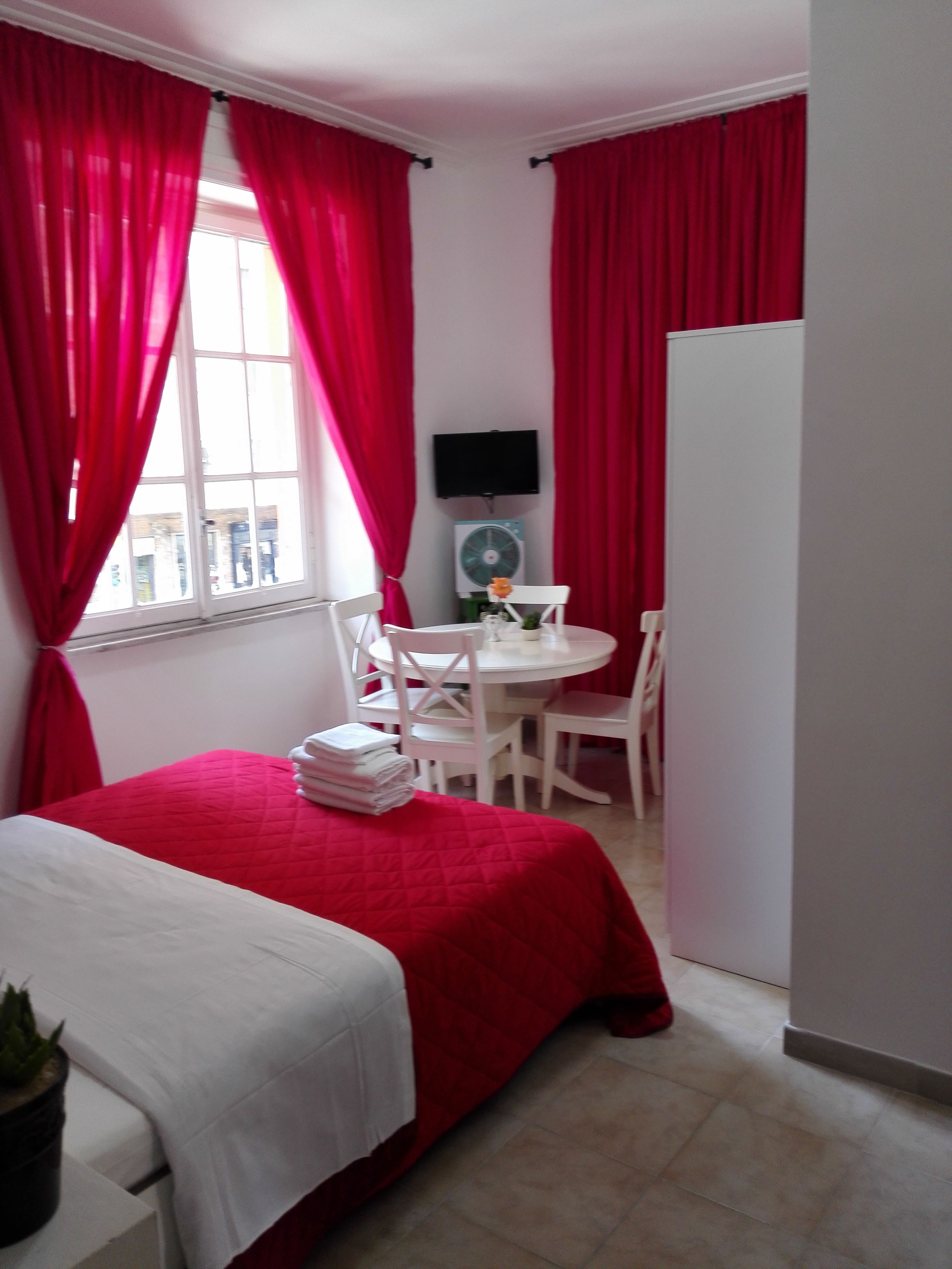 Una habitación con cama, una pequeña mesa con sillas, un televisor y un ventilador.