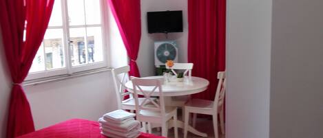 Una habitación con cama, una pequeña mesa con sillas, un televisor y un ventilador.