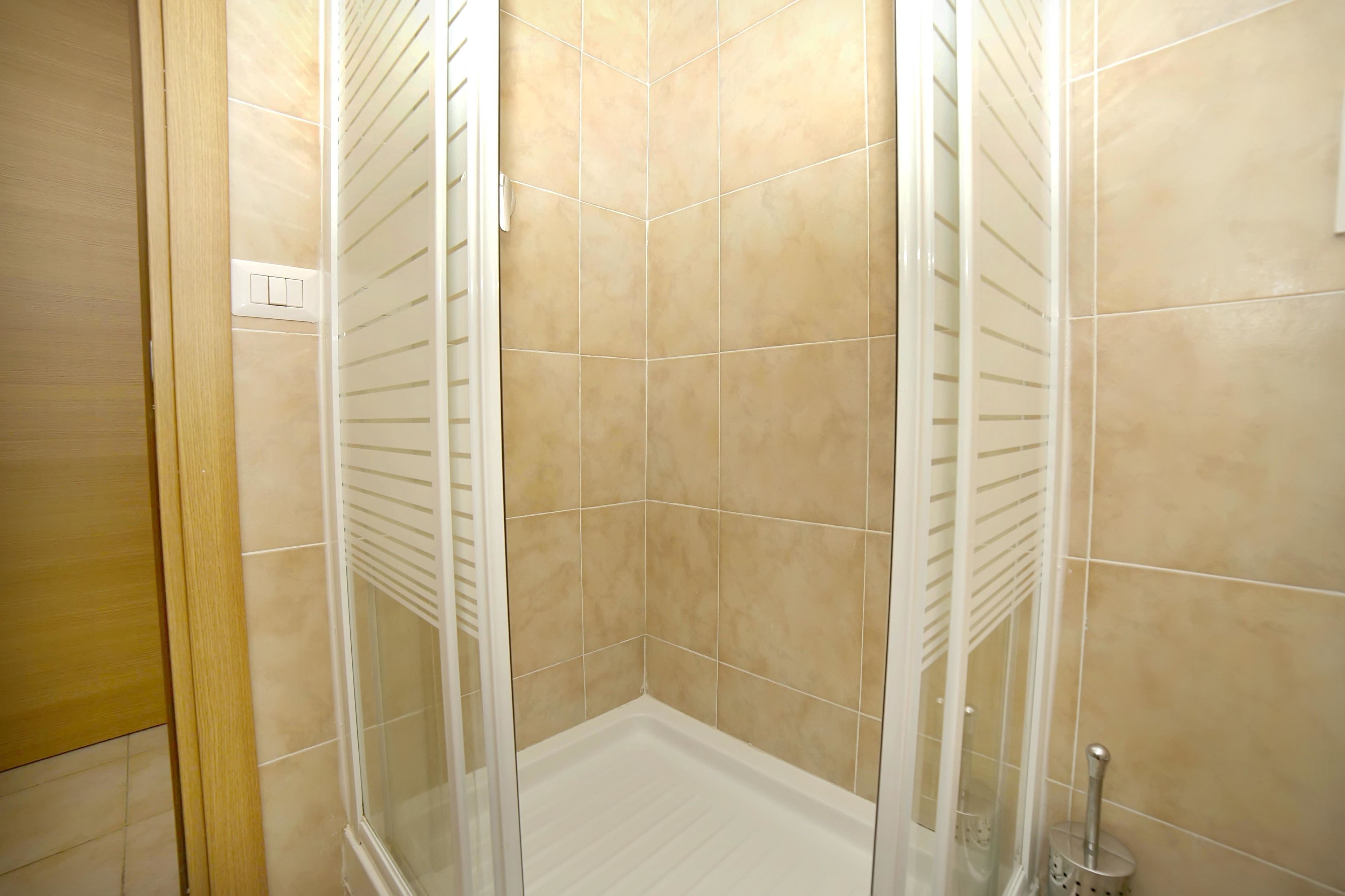 A corner shower with beige tiles and white fixtures.