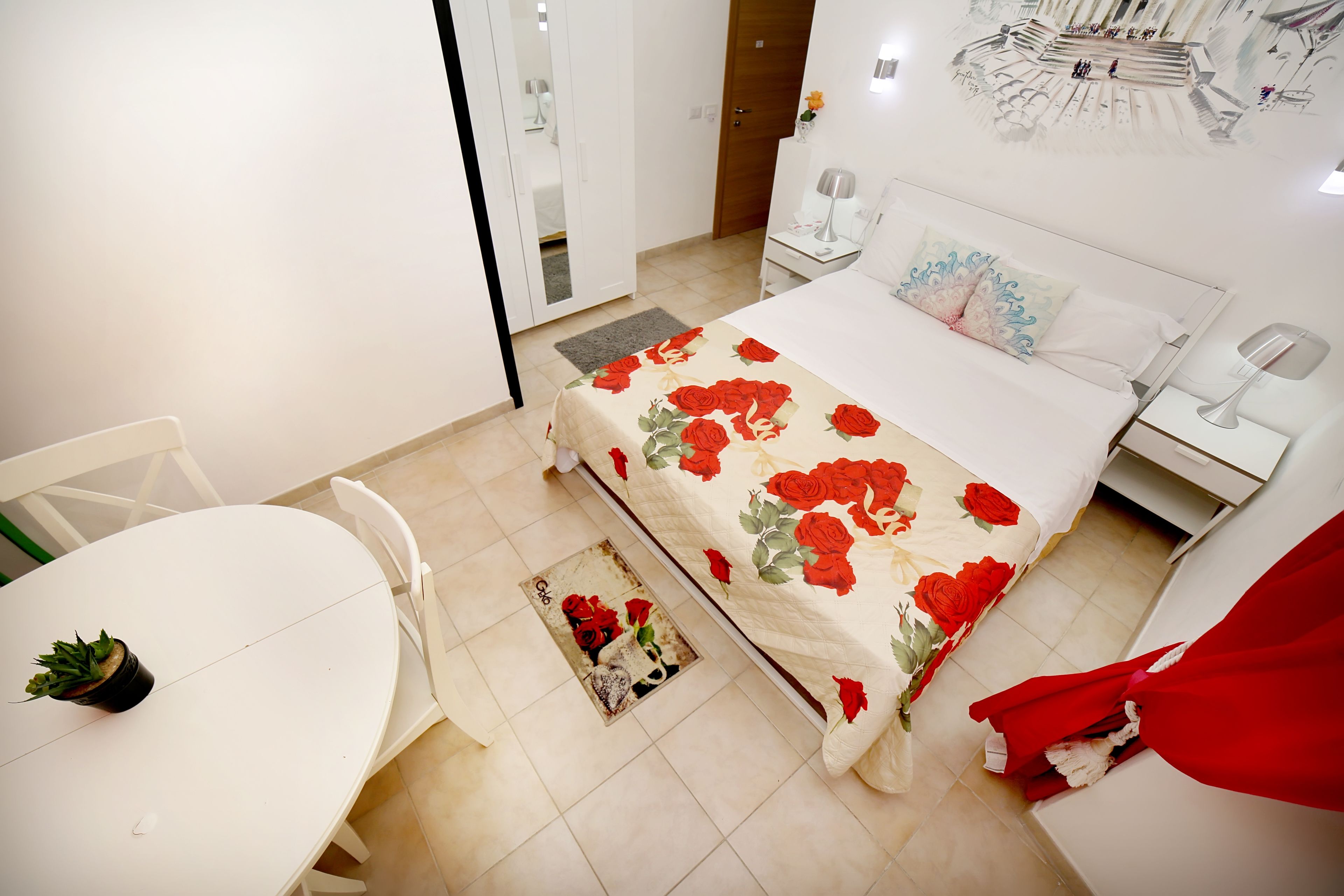 A bedroom with a bed, bedside tables, a nightstand, a chair, a small table with a plant, and a door.