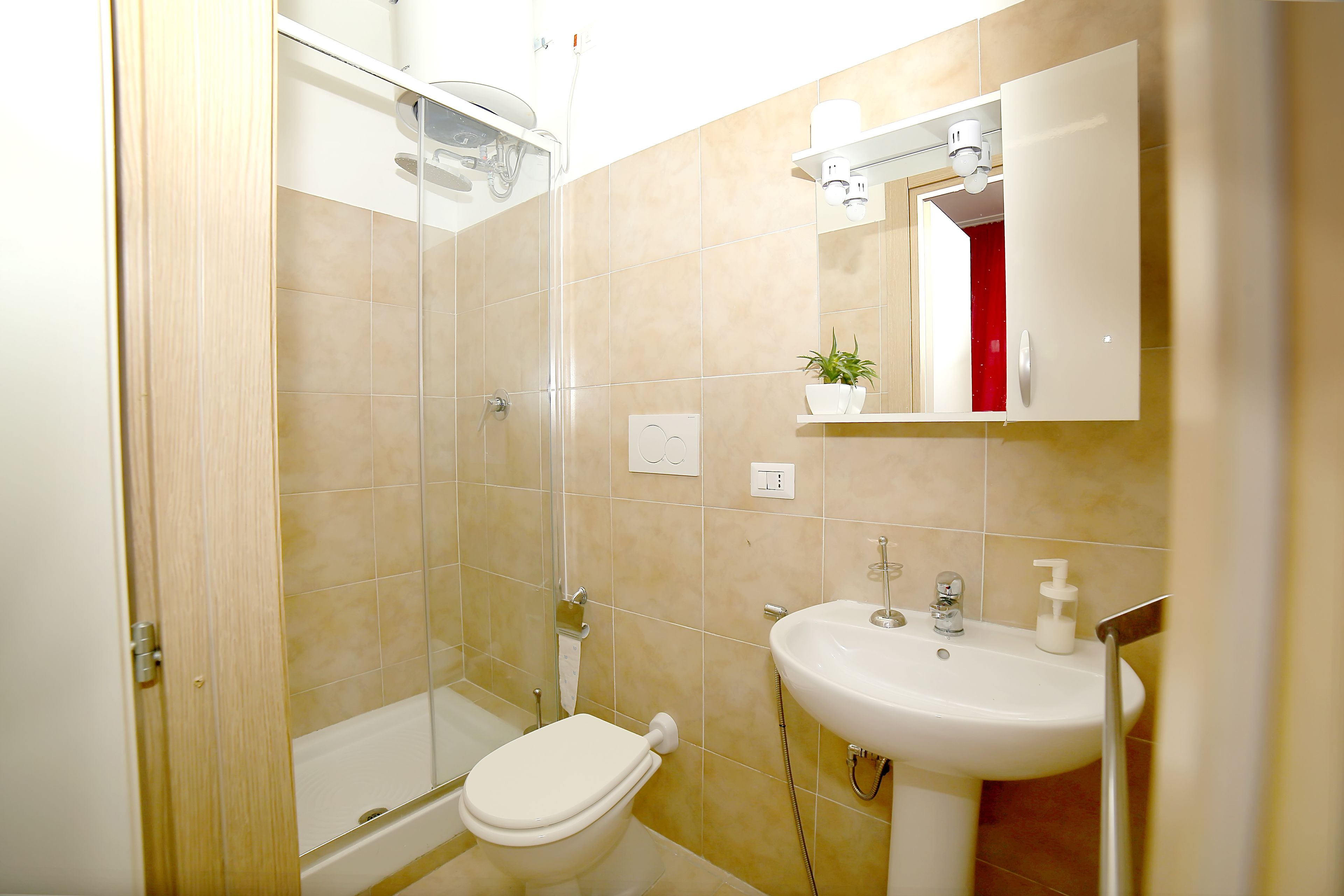 Et badeværelse med bruser, toilet, vask og spejl.
