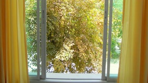 Una habitación con un ventanal grande, cortinas amarillas y una mesa de madera con flores.