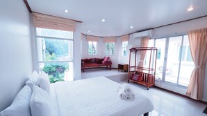 Habitación de hotel con una cama grande, un banco de madera, una cuna y ventanas amplias.