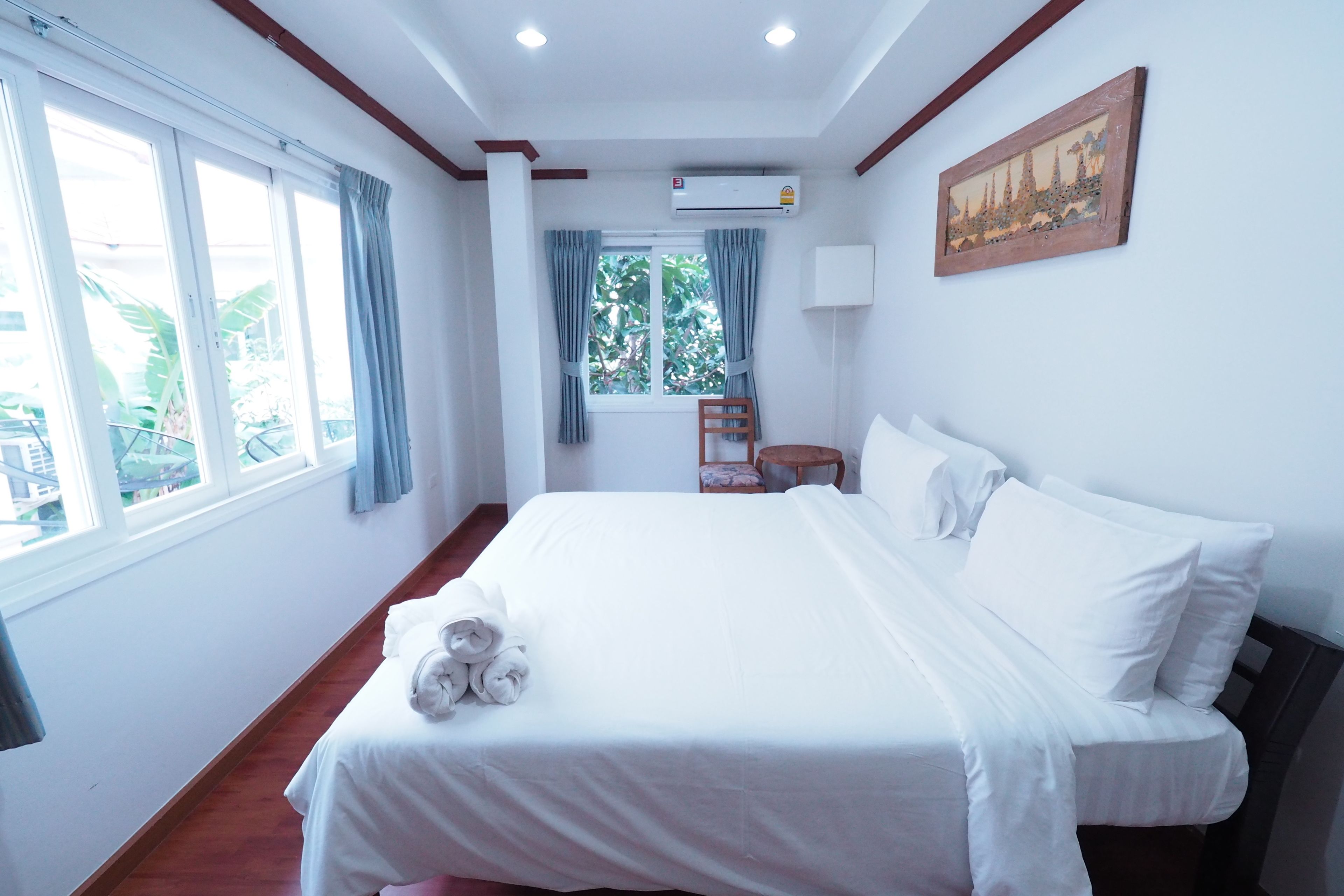 Une chambre d’hôtel avec un grand lit, une fenêtre avec des rideaux, un appareil de climatisation et un tableau au mur.