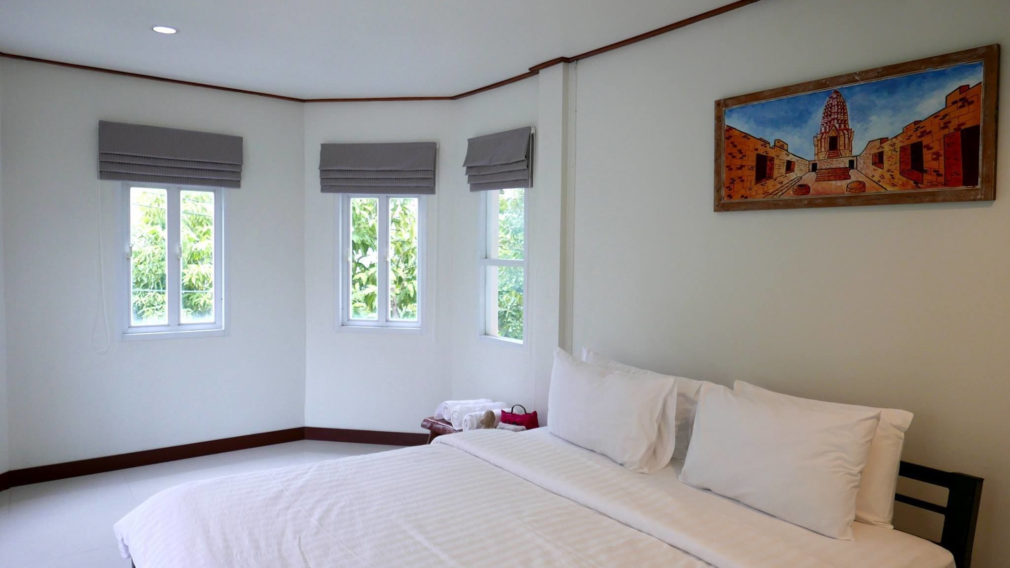 Un dormitorio con una cama grande, tres ventanas y un cuadro en la pared.
