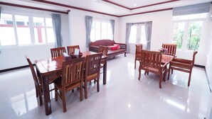 Un comedor amplio con mesa y sillas de madera, ventanas grandes con cortinas, y un sofá rojo al fondo.
