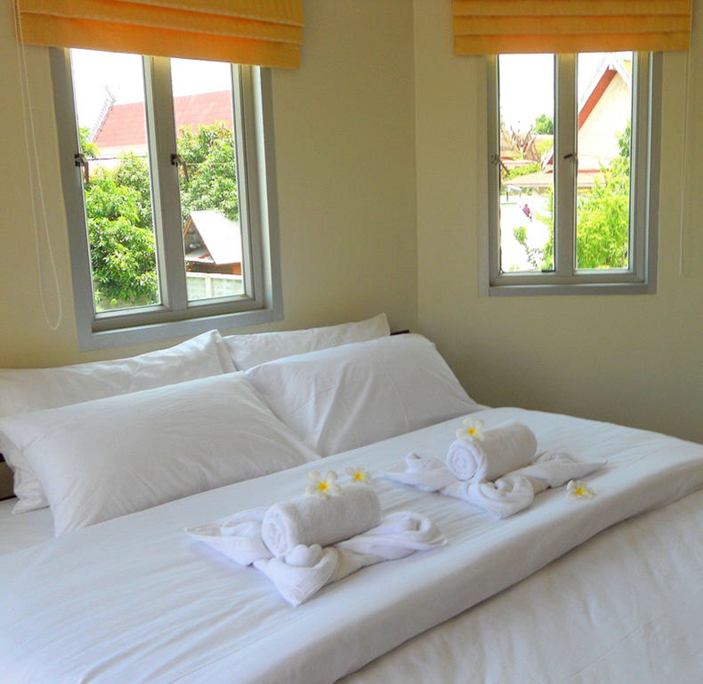 Une chambre d’hôtel avec un grand lit, deux fenêtres équipées de stores et une vue sur la verdure environnante.