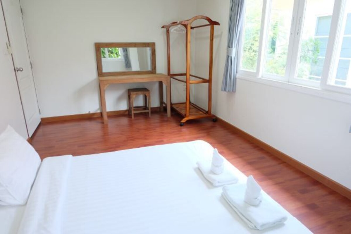 A hotel room with a bed, a wooden desk, a chair, a mirror, and a window with curtains.