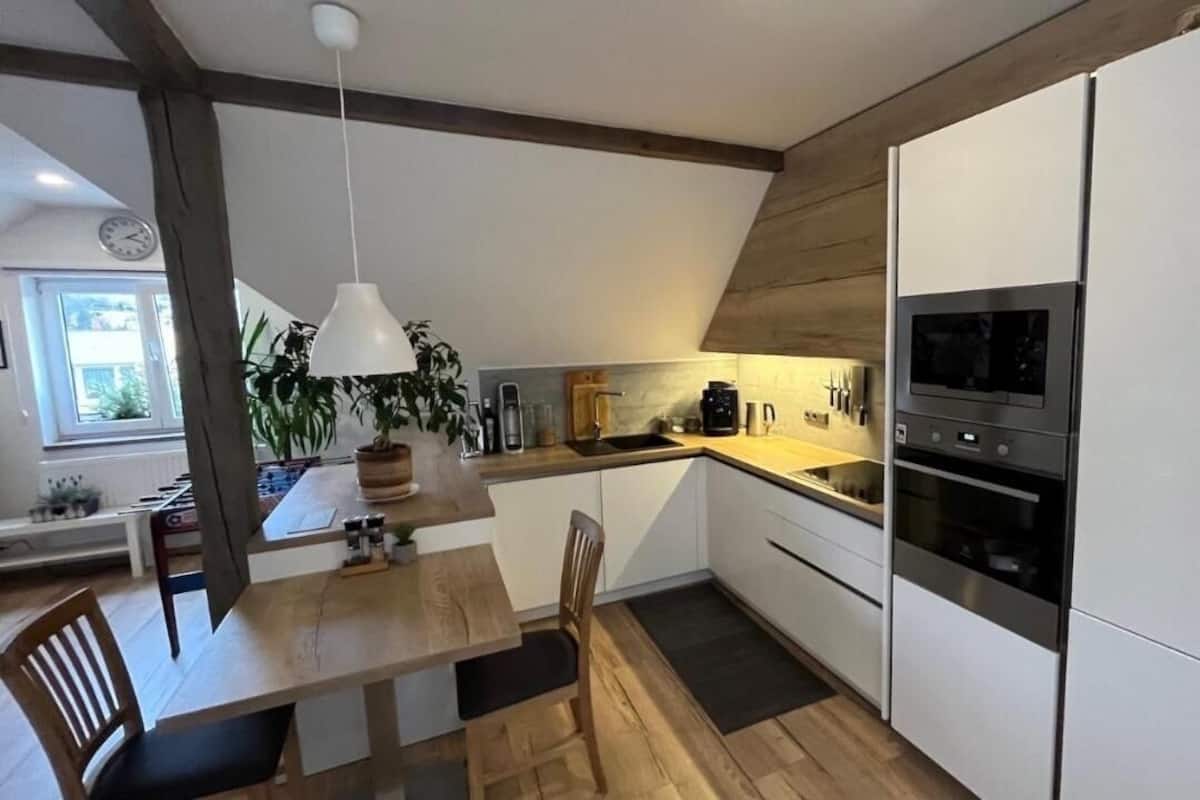 A modern kitchen with white cabinets, a wooden dining table, and a hanging pendant light.