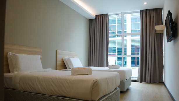 A hotel room with two beds, a large window with curtains, a flat-screen TV mounted on the wall, and a view of a building outside. - Orange Hotels Sri Petaling (Kuala Lumpur)
