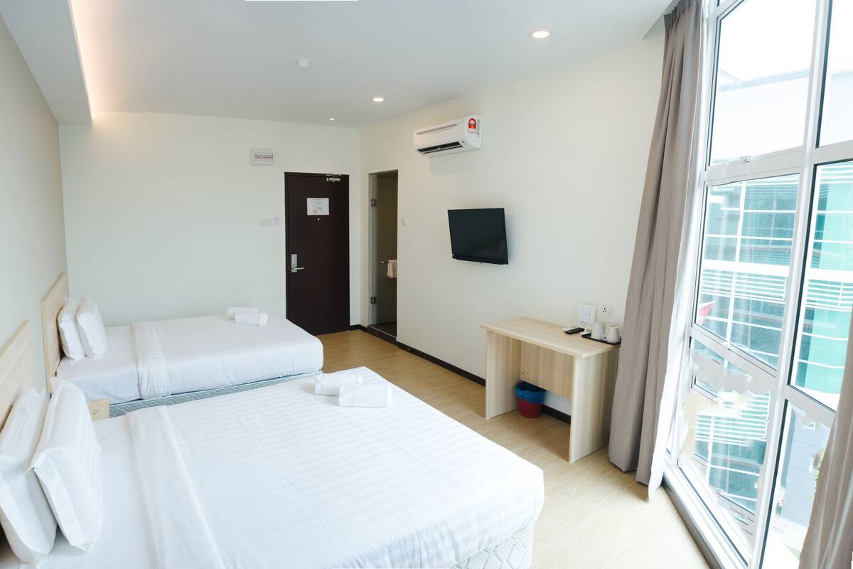 A hotel room with two beds, a desk, a TV, and a window.
