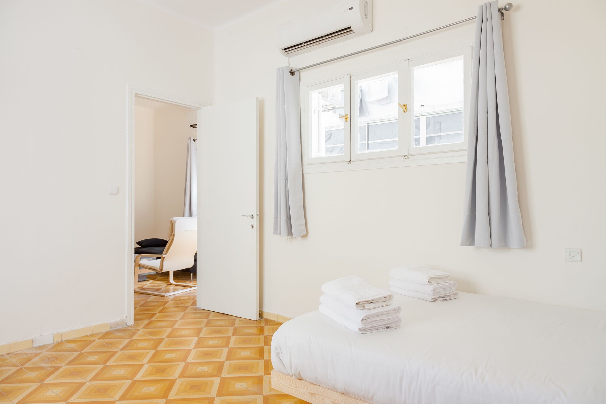 Ein Hotelzimmer mit Bett, Stuhl, einem Vorhangfenster und Fliesenboden.