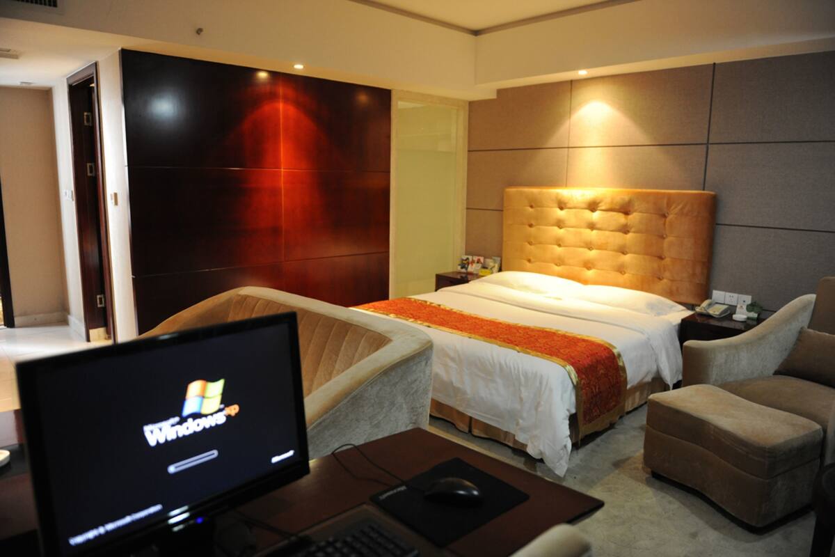 A hotel room with a large bed, a desk with a computer, and a chair.