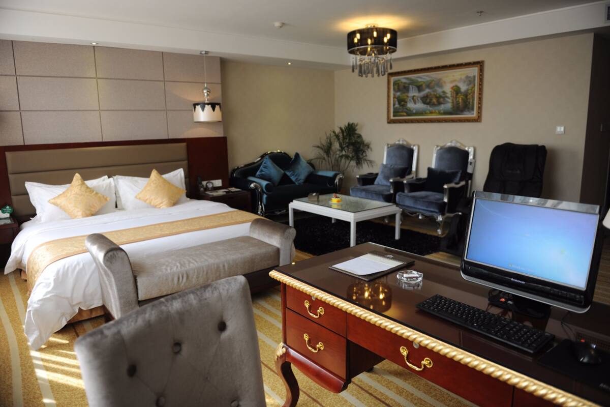 A hotel room with a large bed, a desk with a computer, two armchairs, a coffee table, and a painting on the wall.