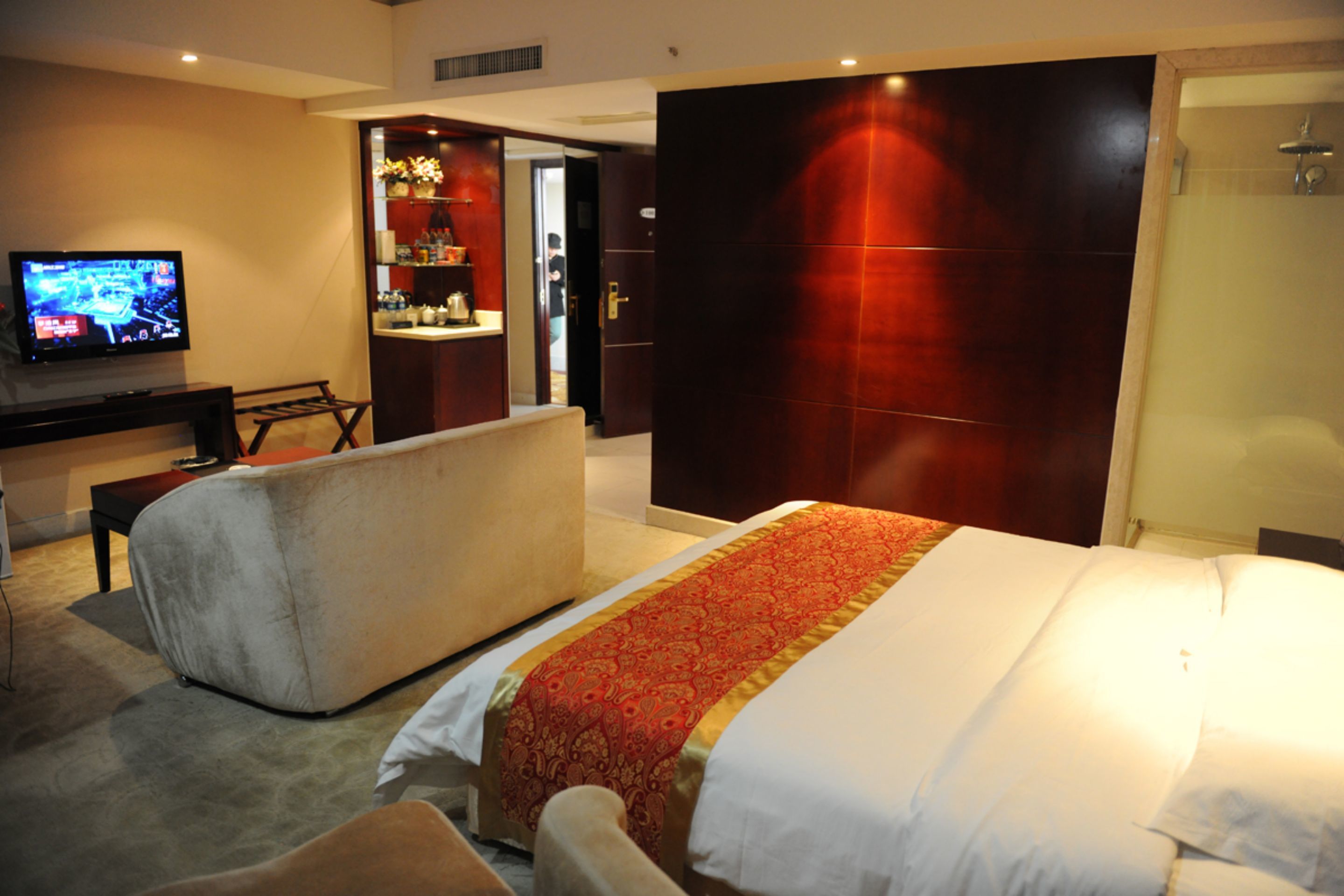 A hotel room with a large bed, a desk with a television, a sofa, and a bathroom with a shower.