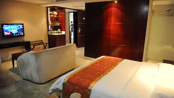 A hotel room with a large bed, a desk with a television, a sofa, and a bathroom with a shower.