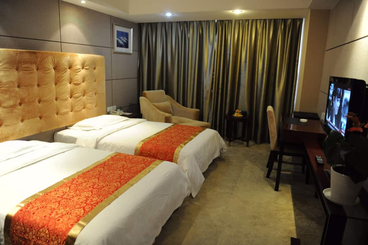 A hotel room with two beds, a desk with a television, and a chair.