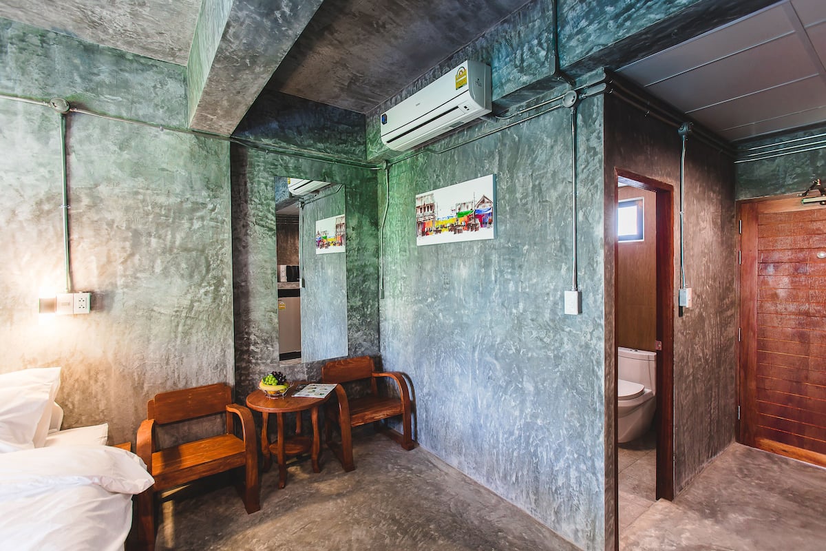 A compact room with a bed, wooden chairs, a small table, and a toilet.