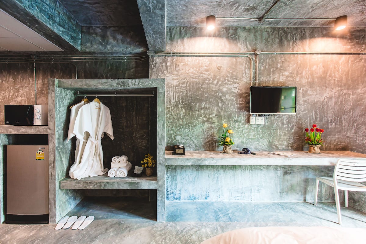 A modern bathroom with a marble countertop, a hanging robe, a small sink, and a TV mounted on the wall.