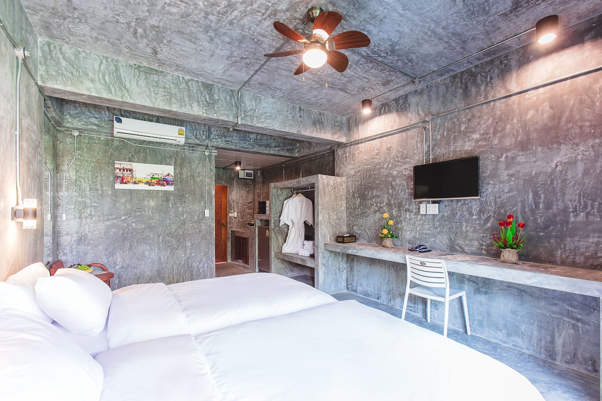 A modern hotel room with a large bed, a desk with a chair, a ceiling fan, and a flat-screen TV mounted on the wall.