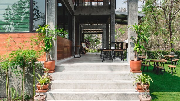 A set of outdoor steps leading to a covered seating area with tables and chairs, surrounded by potted plants and a green lawn. - Stucco Loft Residency (Chiang Mai)