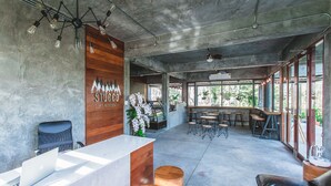 A spacious reception area with a wooden reception desk, a black leather chair, and a seating area with wooden stools and tables. - Stucco Loft Residency (Chiang Mai)