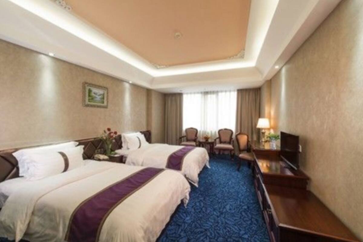 A hotel room with two beds, a desk, a chair, a TV, and a window with curtains.