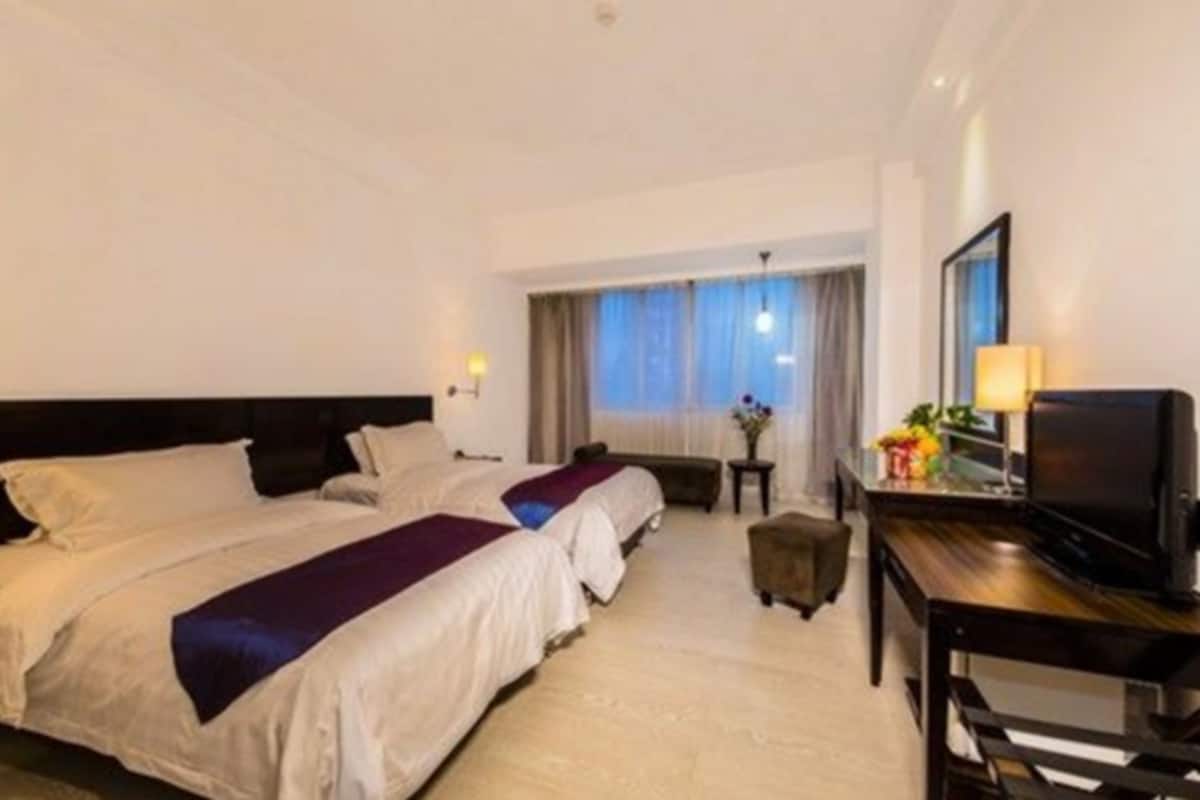 A hotel room with two beds, a desk with a television, and a window with curtains.