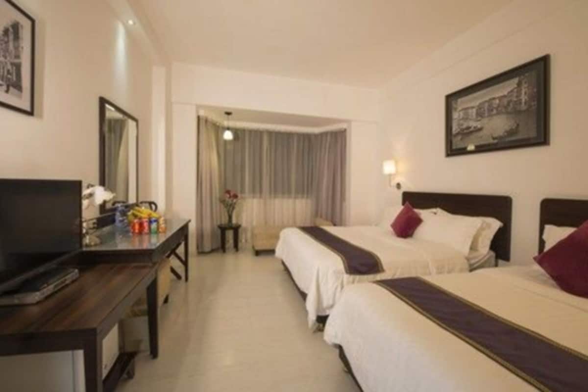 A hotel room with two beds, a desk with a TV, and a window with curtains.