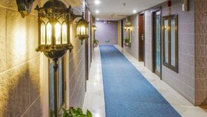 Ein Hotelkorridor mit blauem Teppich, verzierten Wandleuchtern und einem gefliesten Boden.