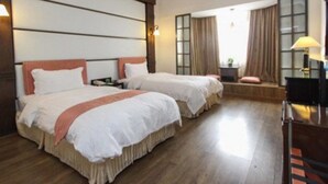 Ein Hotelzimmer mit zwei Betten, Holzboden, einem großen Fenster mit Vorhängen und einem Schreibtisch mit Lampe.